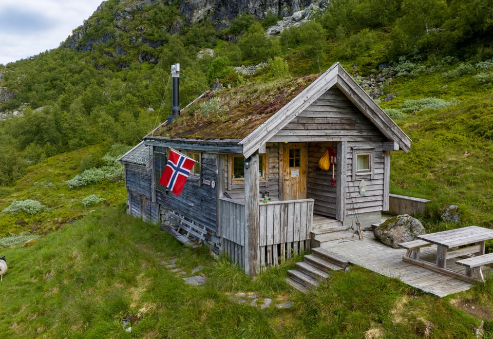 Koselig klassisk hytte med torvtak og norsk flagg utenfor.