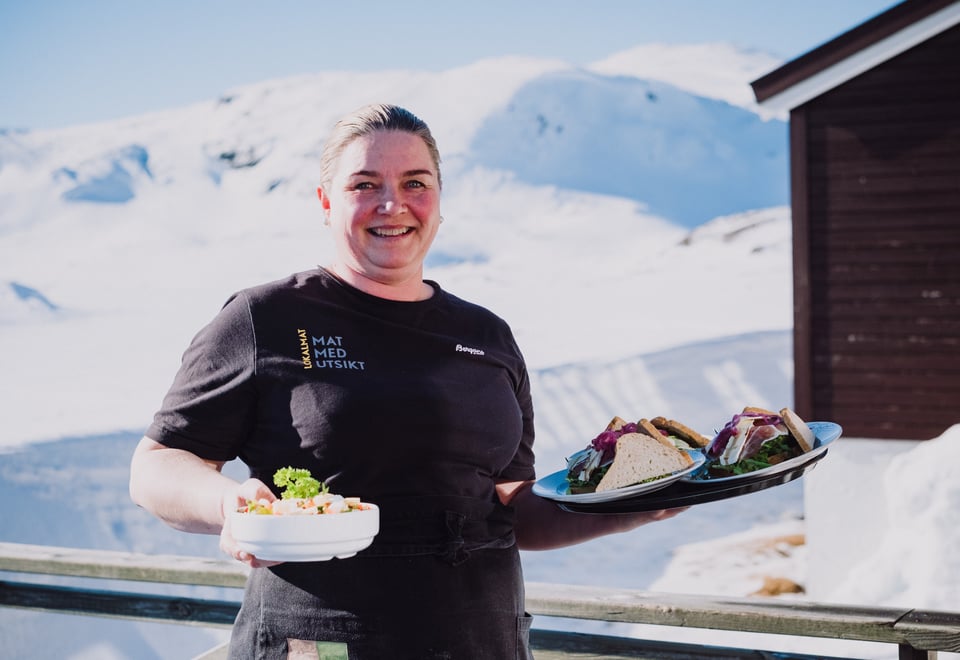 Bestyrer Torill serverer mat ute ved hytteveggen,