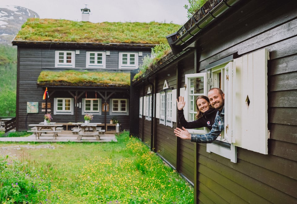 Bilde av to personer som vinker fra vinduet i hytta.