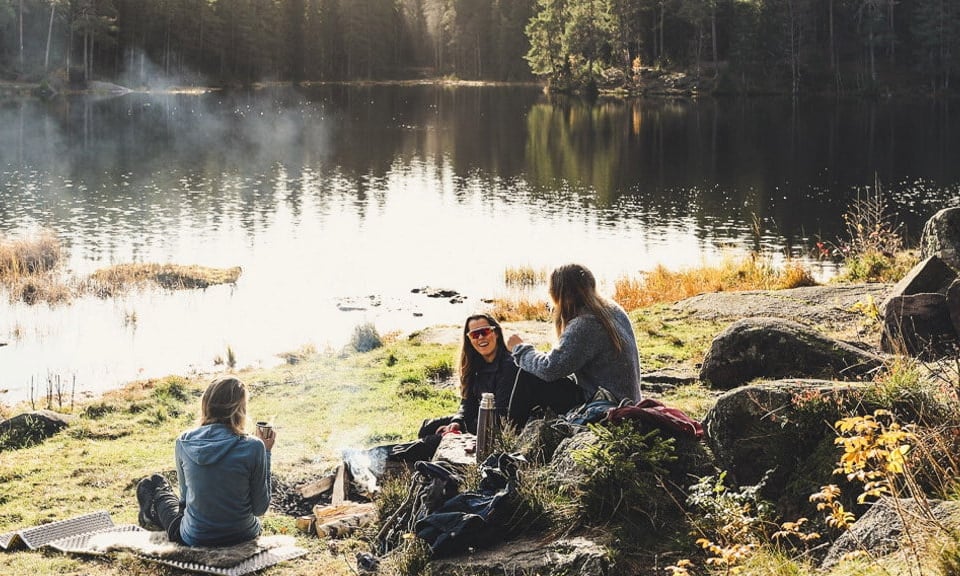 Personer som sitter rundt et bål ved et vann