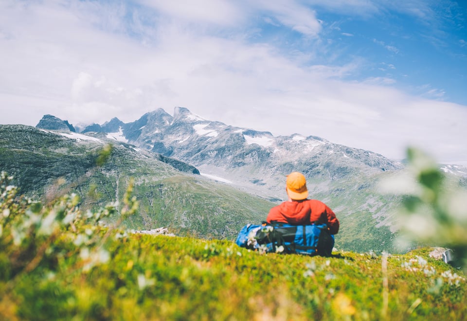 Mann som sitter med rygg mot en sekk og ser på utsikt mot snødekte fjell.