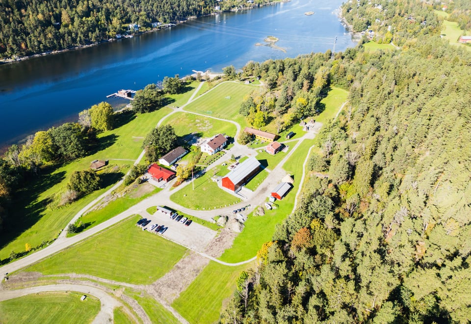 Et dronebilde over landskapet rundt Breivoll Gård, grønne gressletter, Bunnefjorden og grønn skog.