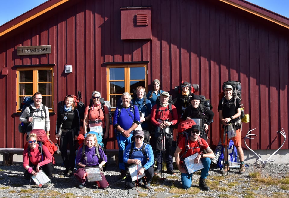 Mennesker samlet med turtøy, kart og kompass utenfor en hytte
