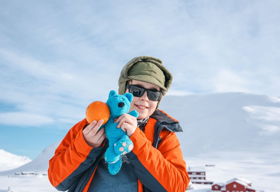 En liten blå bamse i snøen og en appelsin.