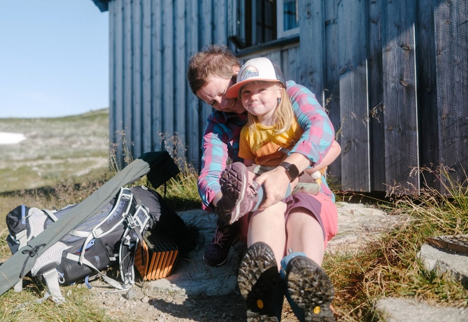 En mor og en datter sitter foran en hyttevegg og tar på seg fjellsko
