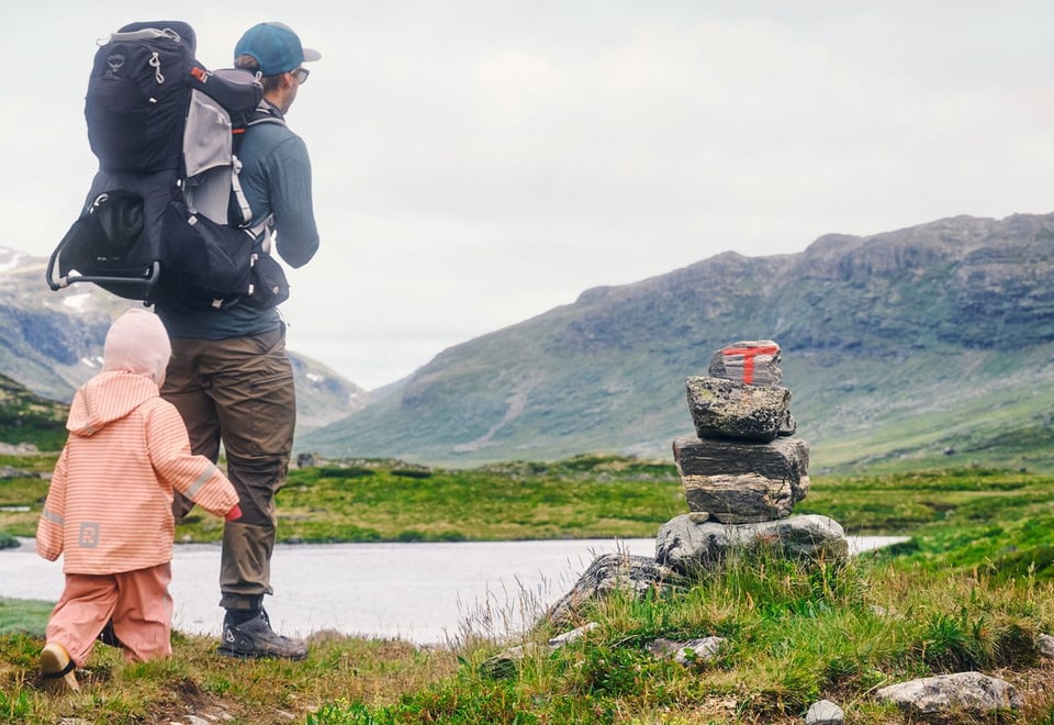En voksen og et barn går på tur i Skarvheimen forbi en varde merket med rød T