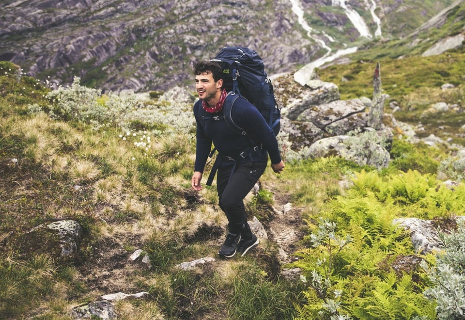En gutt går i et bratt fjellandskap på sommeren
