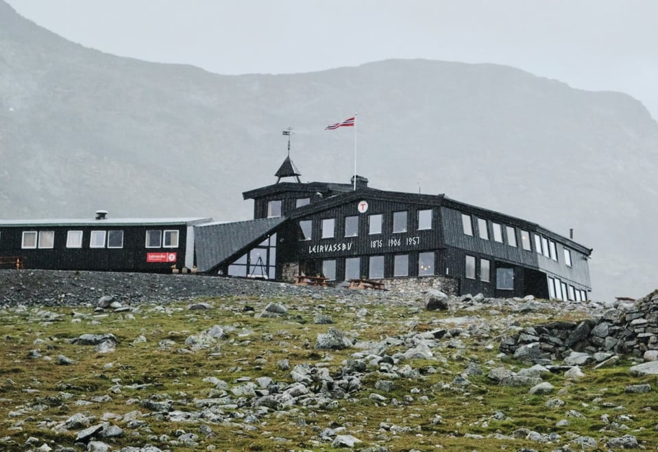 En fjellhytte i et golt sommerlandskap hvor det norske flagget blåser i vinden