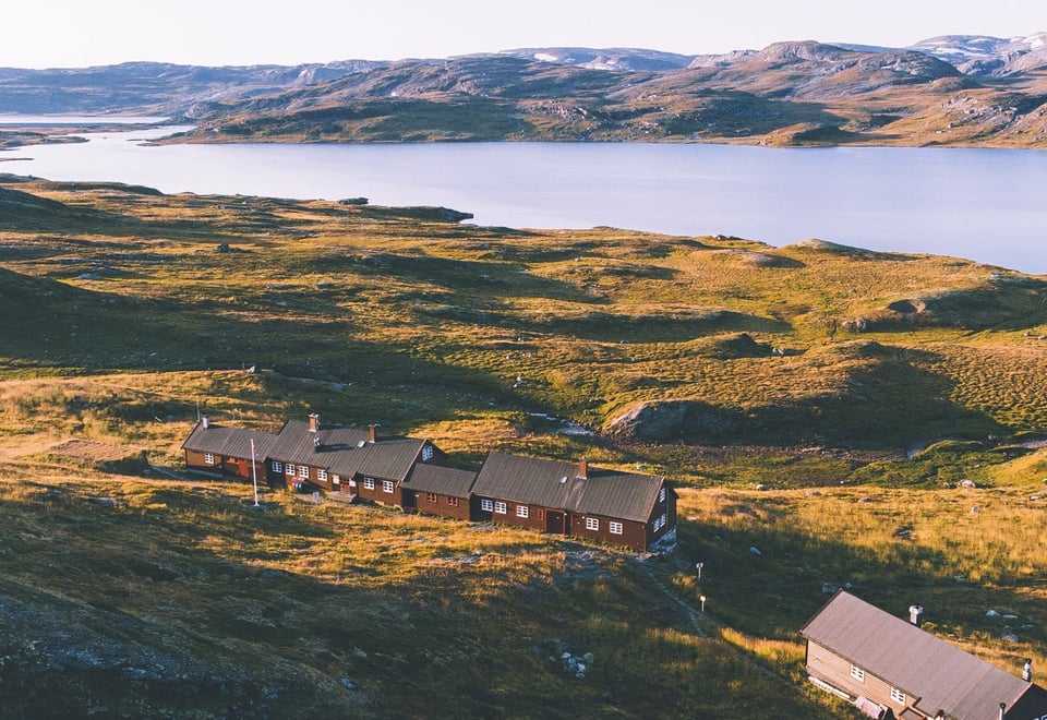 En hytte foran et vann i et sommerlig fjellandskap