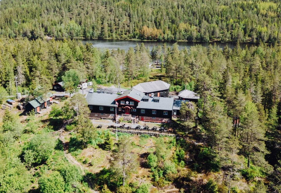 En mørkebrun hytte sett ovenfra med drone i et grønt skogslandskap