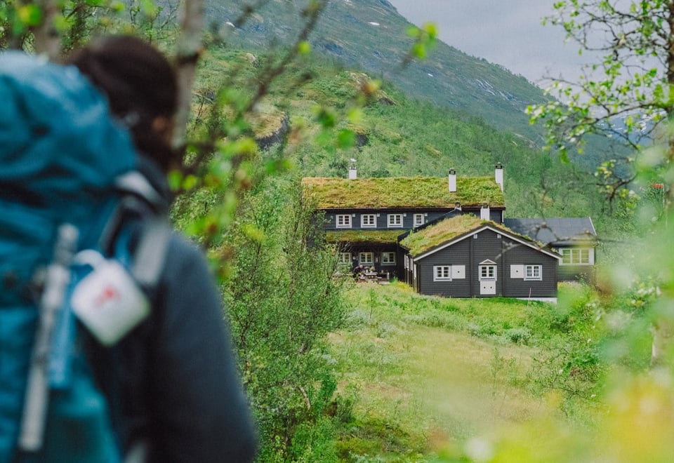 Person med ryggsekk som ser på en hytte i det fjerne