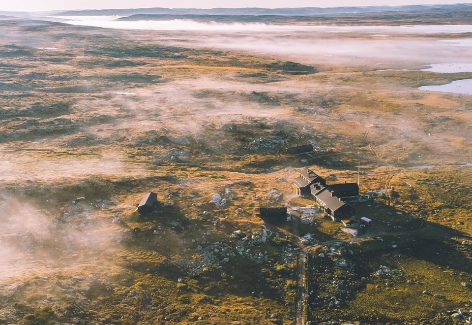 Et tåkelagt fjellandskap med en hytte i fjellet om sommeren