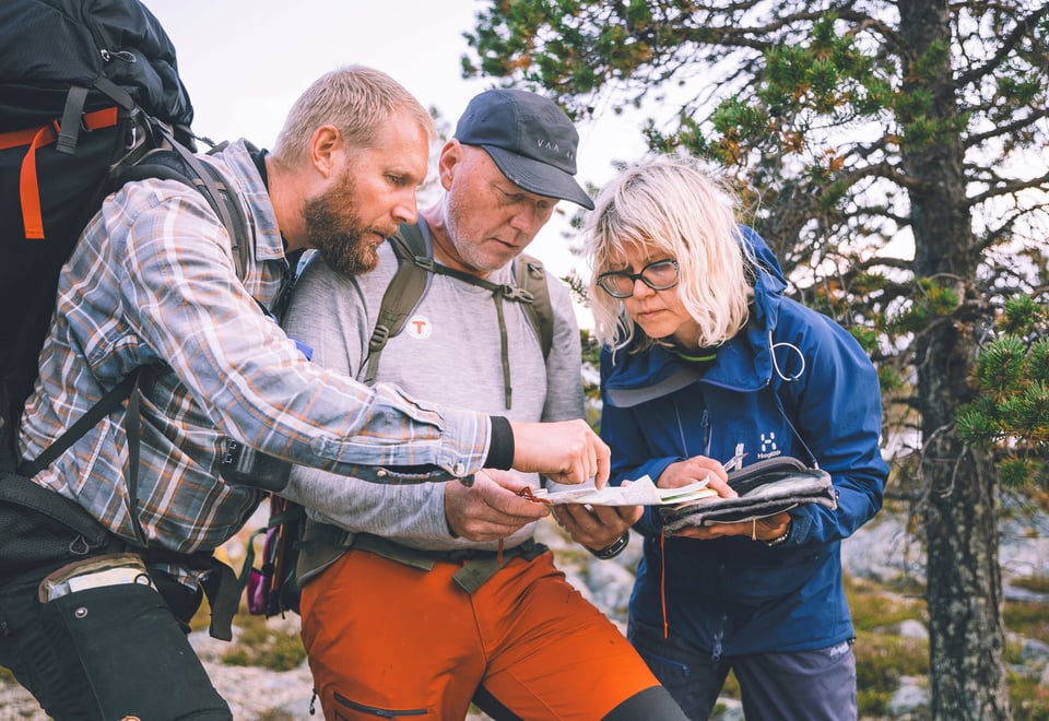 Tre mennesker studerer kart i skogen