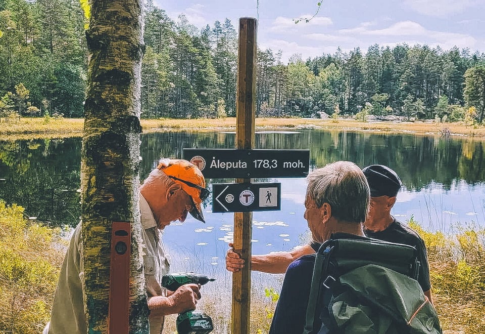 Tre menn som setter opp et turskilt ved et vann.