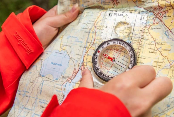 En person med rød jakke holder kart og kompass.