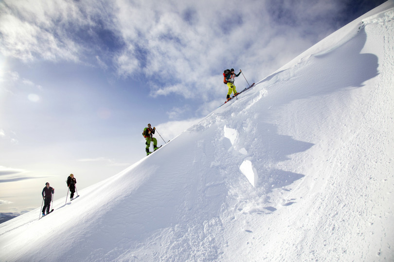 Fire skiløpere går oppover en fjellside, langs en snøskavl.