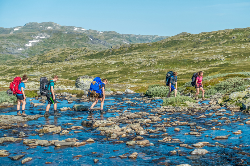 Ungdommer med tursekk krysser vann på fjellet