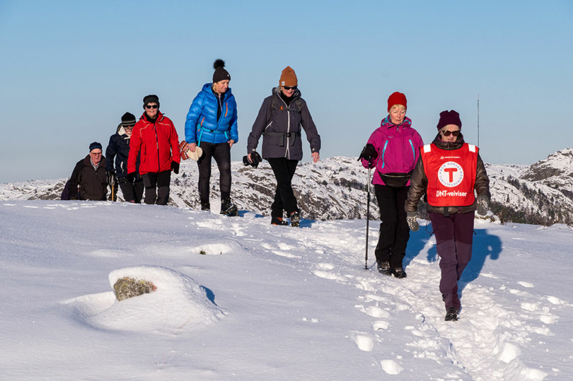 Et turfølge går til fots i snøen over en liten høyde.
