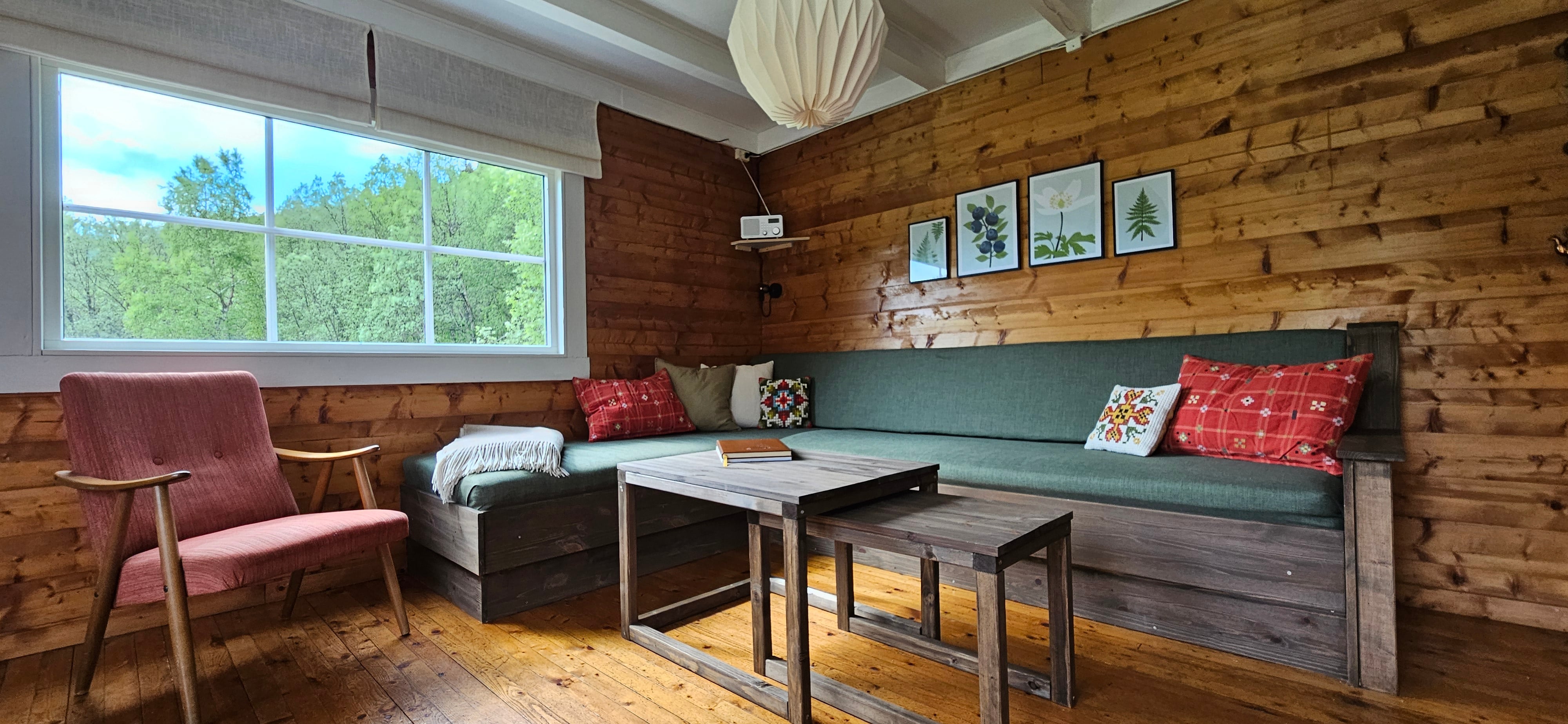 Inventar av hytte med sofa trukket i gr&oslash;nt stoff med fargede pynteputer.