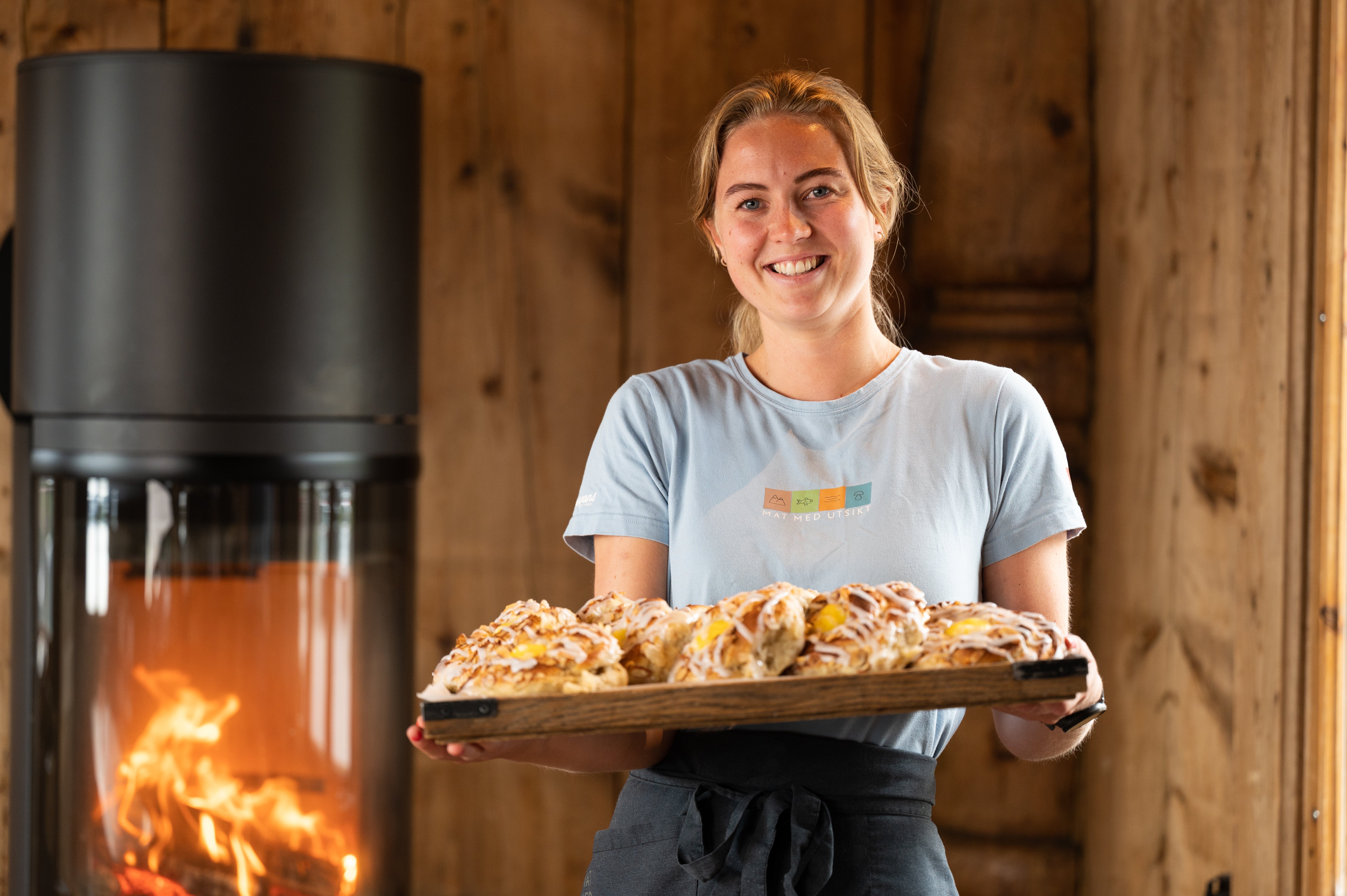 Foto. Jente holder et brett med boller. Peis i bakgrunnnen.