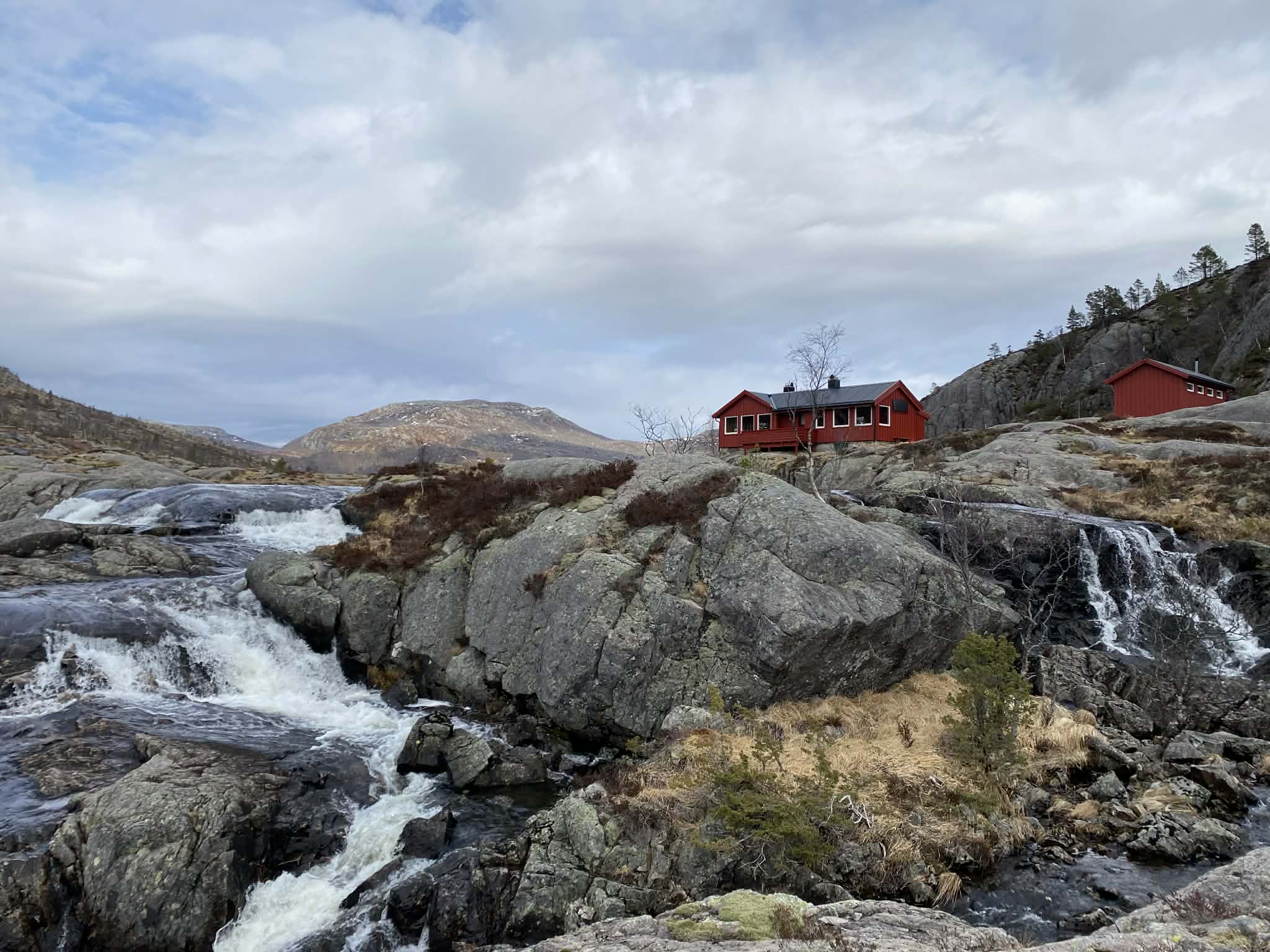 R&oslash;d hytte og fjell, ved en liten elv