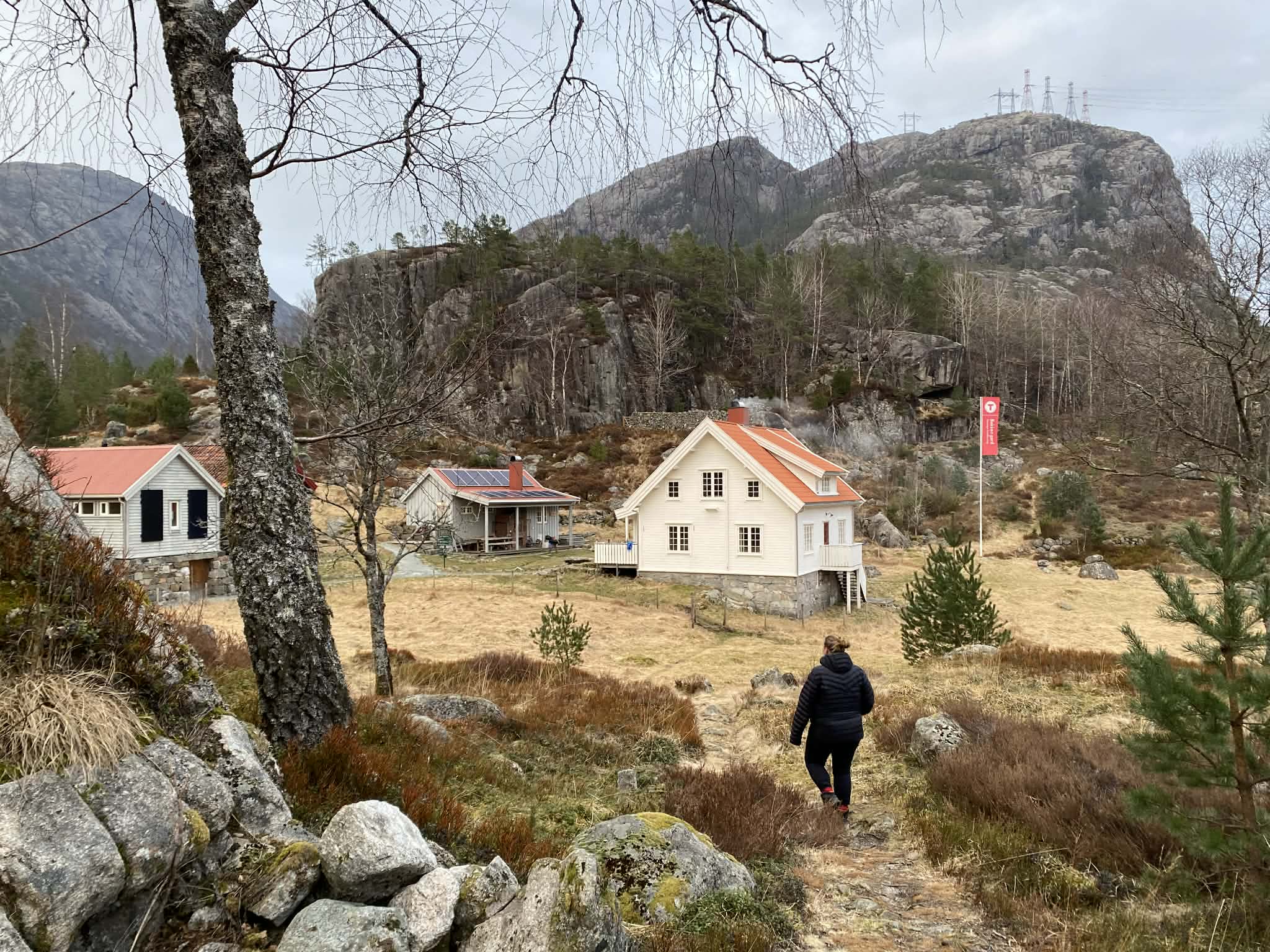 Person som g&aring;r mot hvit hytte i naturen