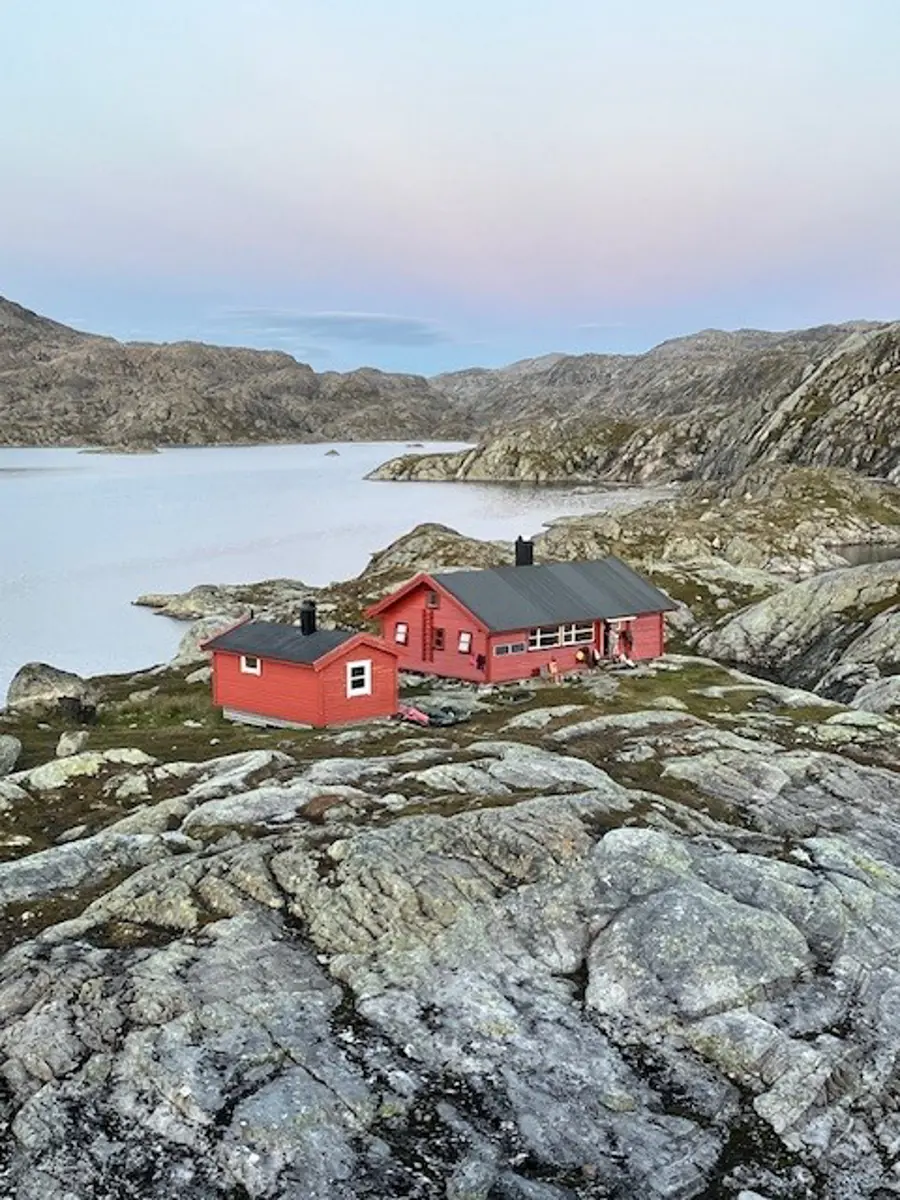 Krossvatn. Rød hytte som ligger mellom bare fjellknauser. Det er et vann bakenfor hytta. 