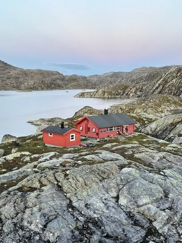 Krossvatn. Rød hytte som ligger mellom bare fjellknauser. Det er et vann bakenfor hytta. 