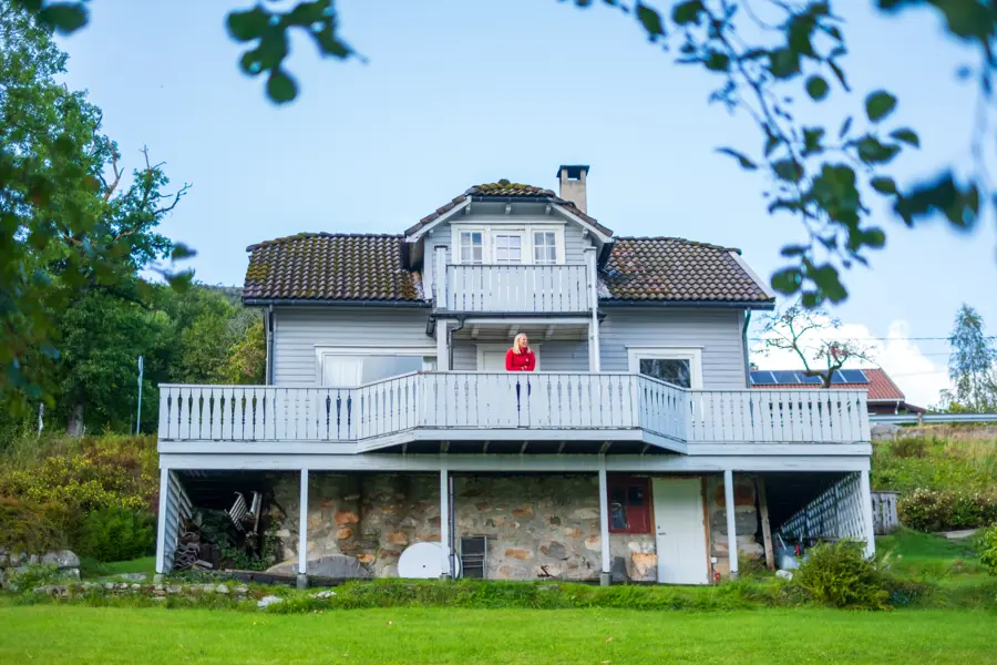 Nodhagen Turisthytte. Grått hus. Det står en jente i rød genser på verandaen. 