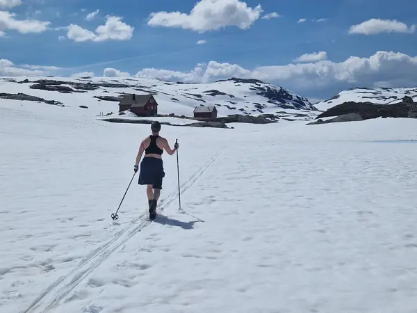 en dame som går på ski i sol og shorts. Hytta Sandvatn i bakgrunnen. 