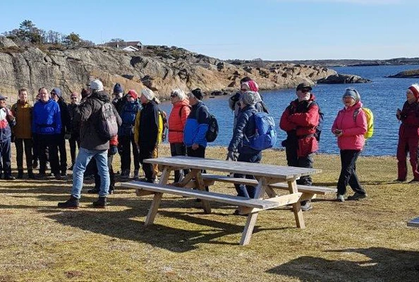 Mennesker og benk på grasslette ved sjøen