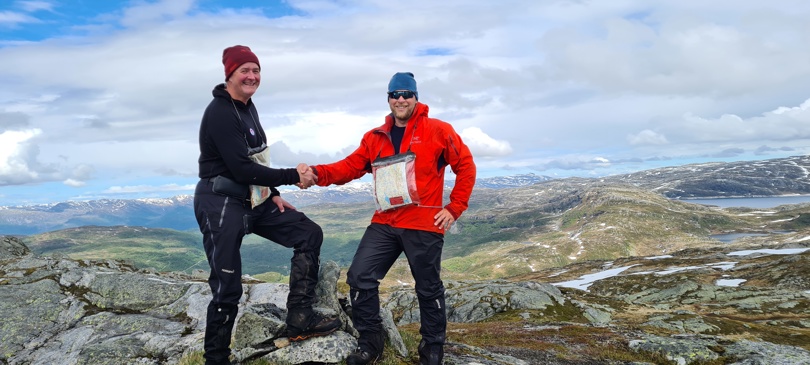 To menn står på fjelltopp og tar hverandre i hendene.