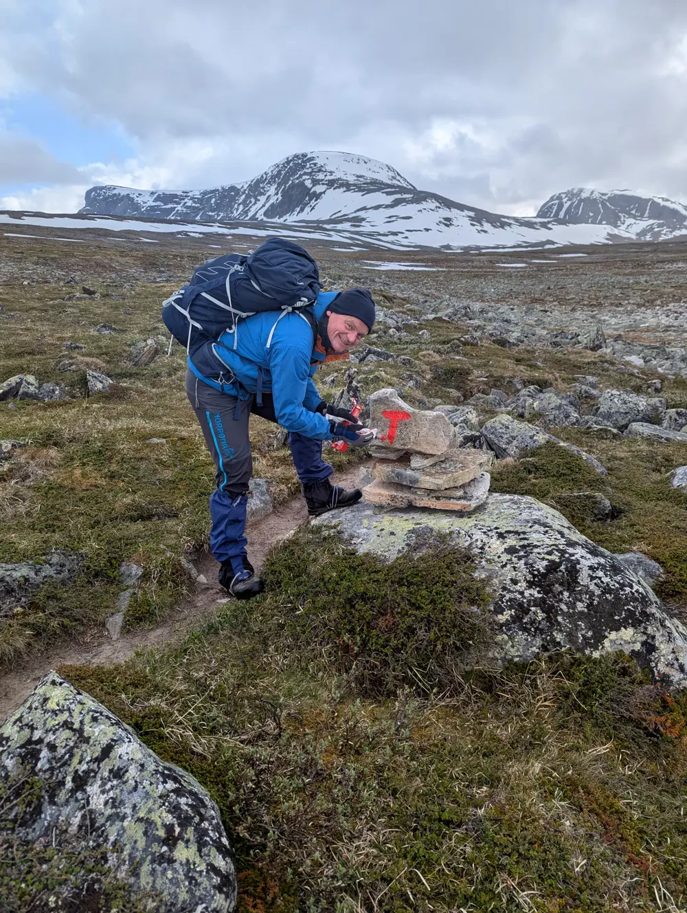 Mann maler rød T på stein langs sti i fjellet