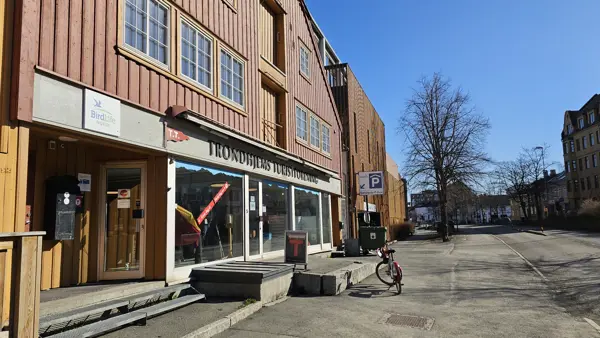 Fasaden av en brygge-bygning i Trondheim sentrum, plankene malt i en gul-oransje farge, og navnet "Trondhjems Turistforening" står over front-vinduene.