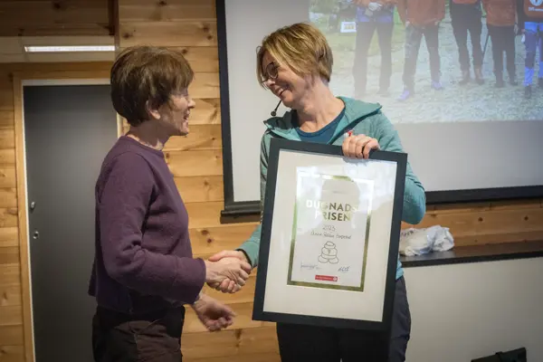 En kvinne overrekker en plakett til en annen kvinne.
