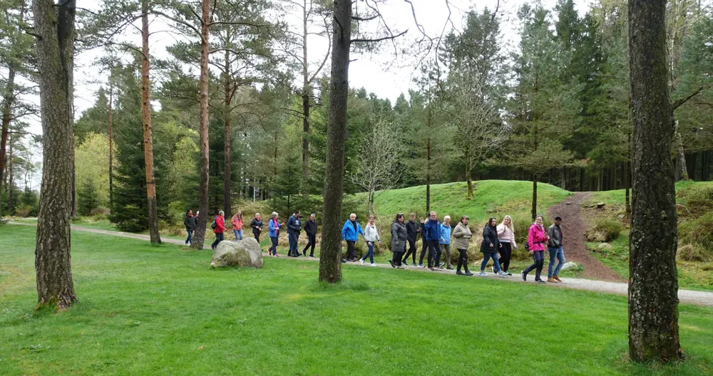 Bak noen trær går en gruppe voksne mennesker på en tursti