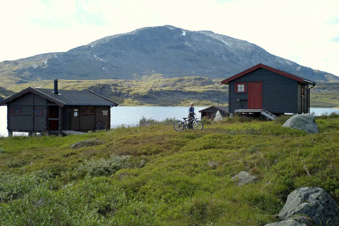 To hytter ved vann med fjell i bakgrunnen