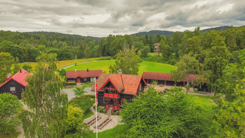 Dronebilde over området. Sommer. Hovedhus i front.