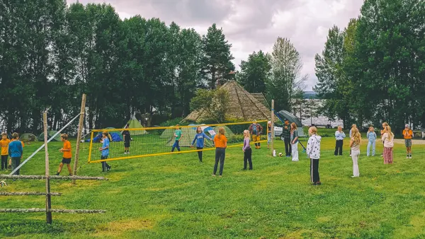 Barn spiller volleyball på gresset. Telt i bakgrunnen.