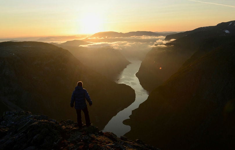 Person står foran solnedgang og ser på fjorden under seg.