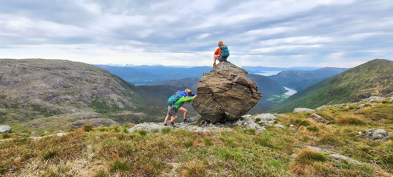 Noen barn dytter på en stor stein og en gutt sitter på toppen.