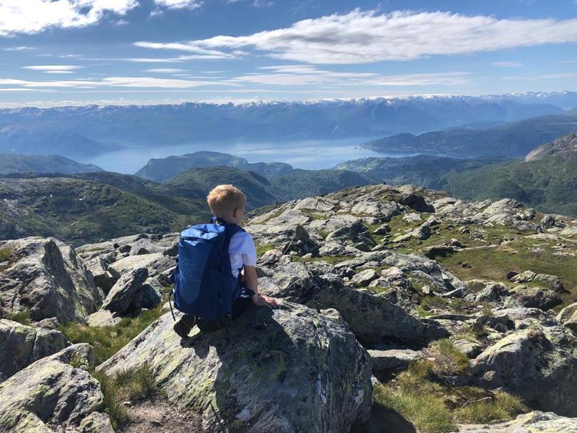 En gutt sitter og ser utover karrig høyfjell og et vann i det fjerne.
