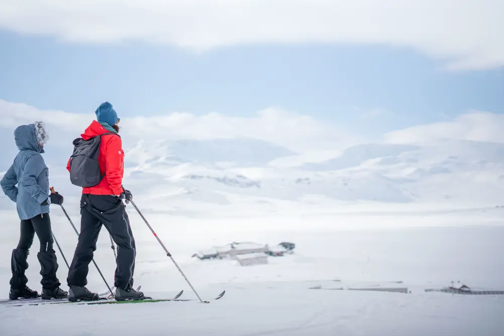 to personer på ski som ser utover Finsehytta og Finsevannet mot Hardangerjøkulen