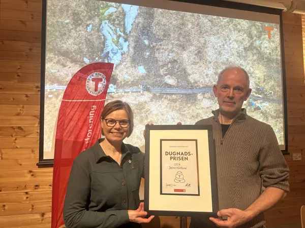 Jostein Nordland mottar diplom for dugnadsprisen 2024 fra styreleder Gunhild Holtet Eie. I bakgrunnen vises en presentasjon i anledning prisutdelingen.
