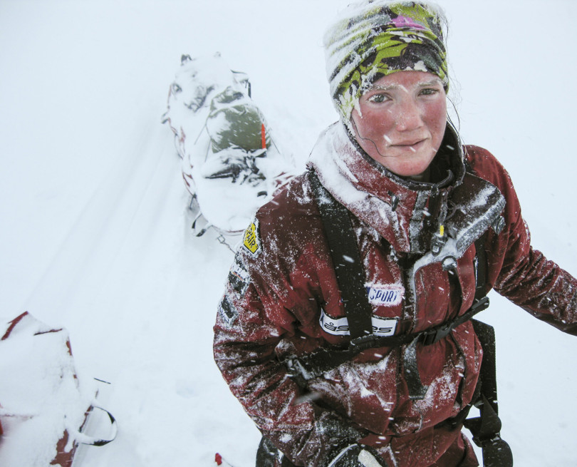 Person i rød jakke trekker en pulk i tett snødrev.