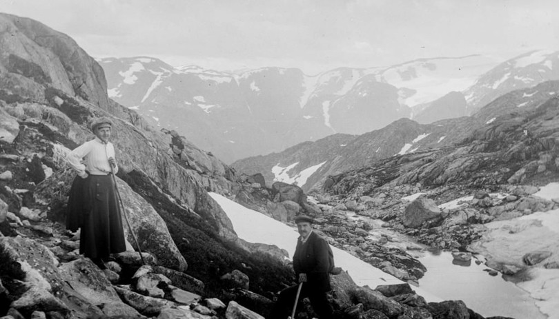 Gammelt sort/hvitt-foto av mann og dame på tur opp en fjellside.