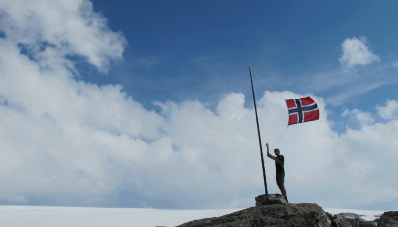 Person heiser det norske flagget i en liten flaggstang på toppen av en steinknaus.