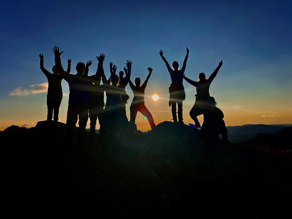 En gruppe personer i siluett på fjelltopp.