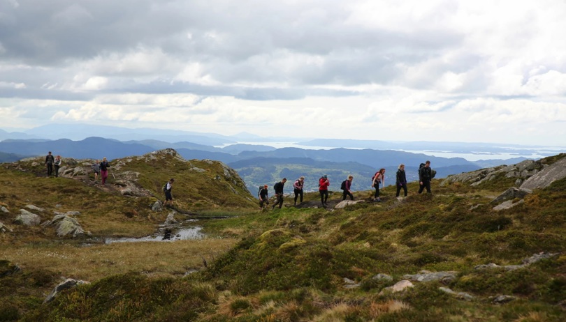 En rekke med mennesker går over et viddelandskap i fjellet.