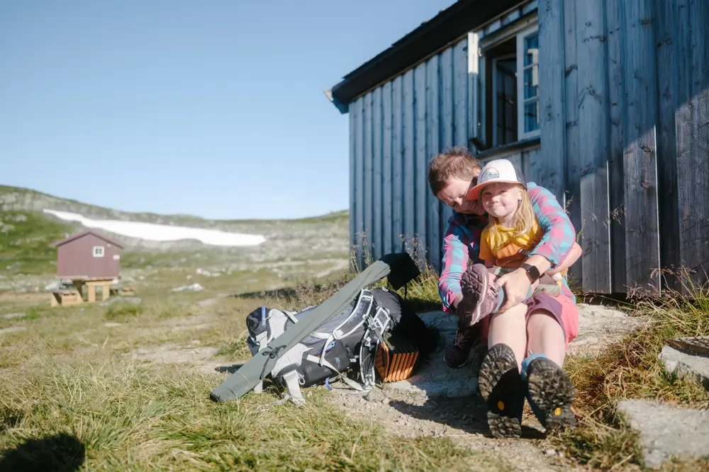 Mor og barn sitter foran hytte i fjellet